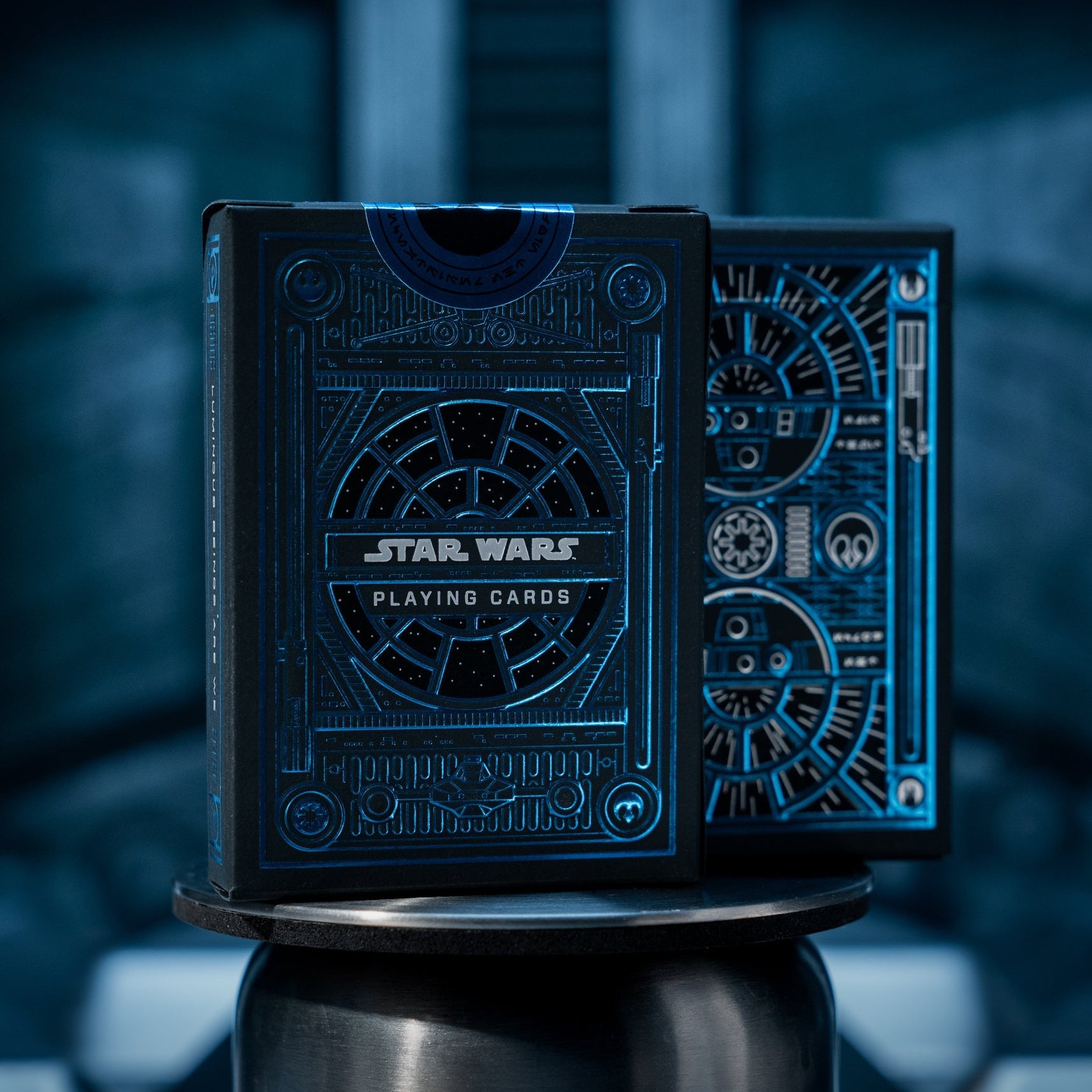 A deck of Star Wars themed playing cards with a blue design, featuring character illustrations and embossed foil details, displayed in a way that mimics the Millennium Falcon's cockpit window.